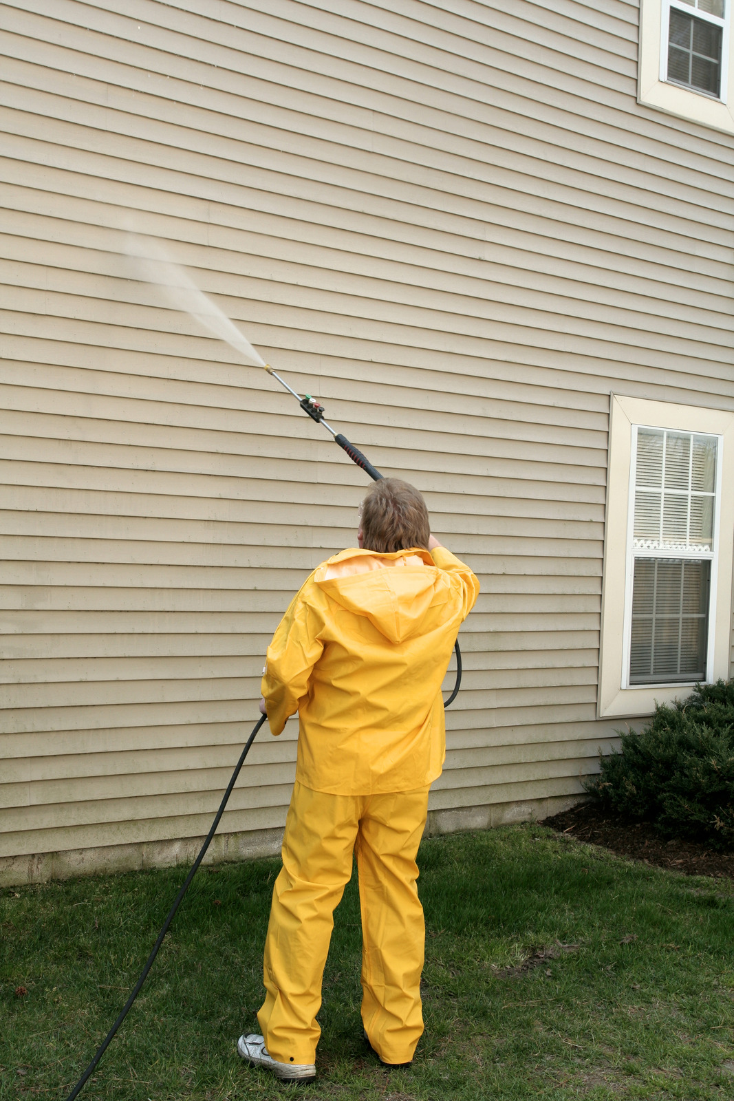 Worker pressure washing light-colored vinyl siding on a residential home